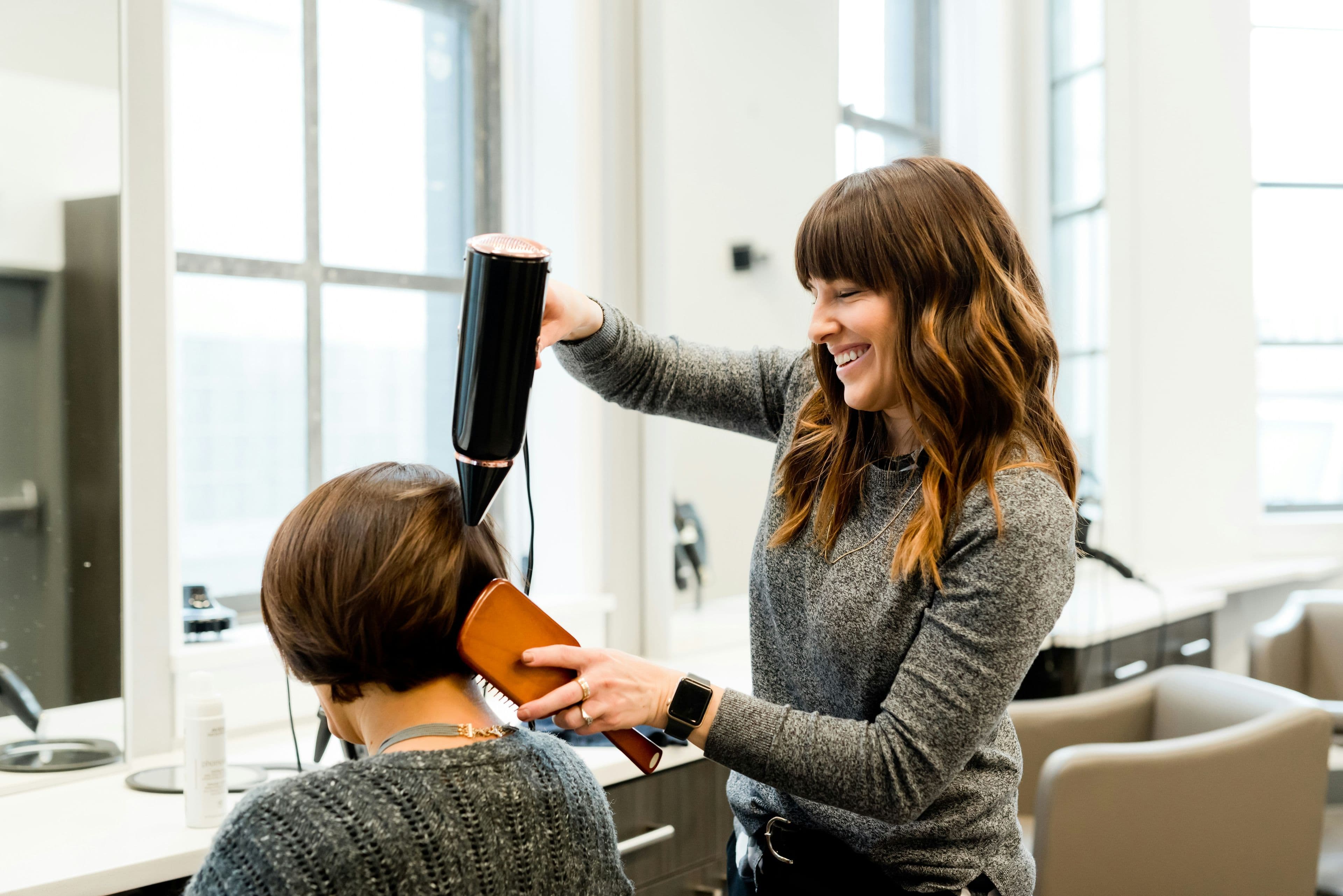 Estilista sonriendo mientras seca y peina el cabello de una clienta en un salón de belleza