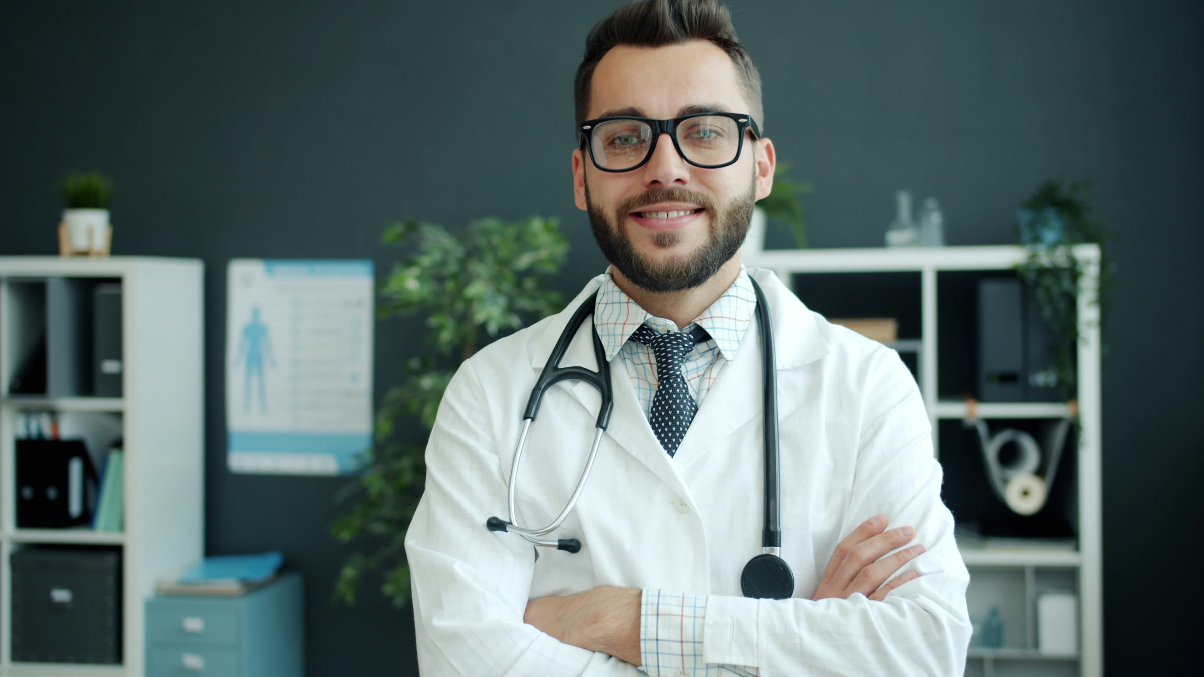 Médico sonriendo con bata blanca y estetoscopio en su consultorio