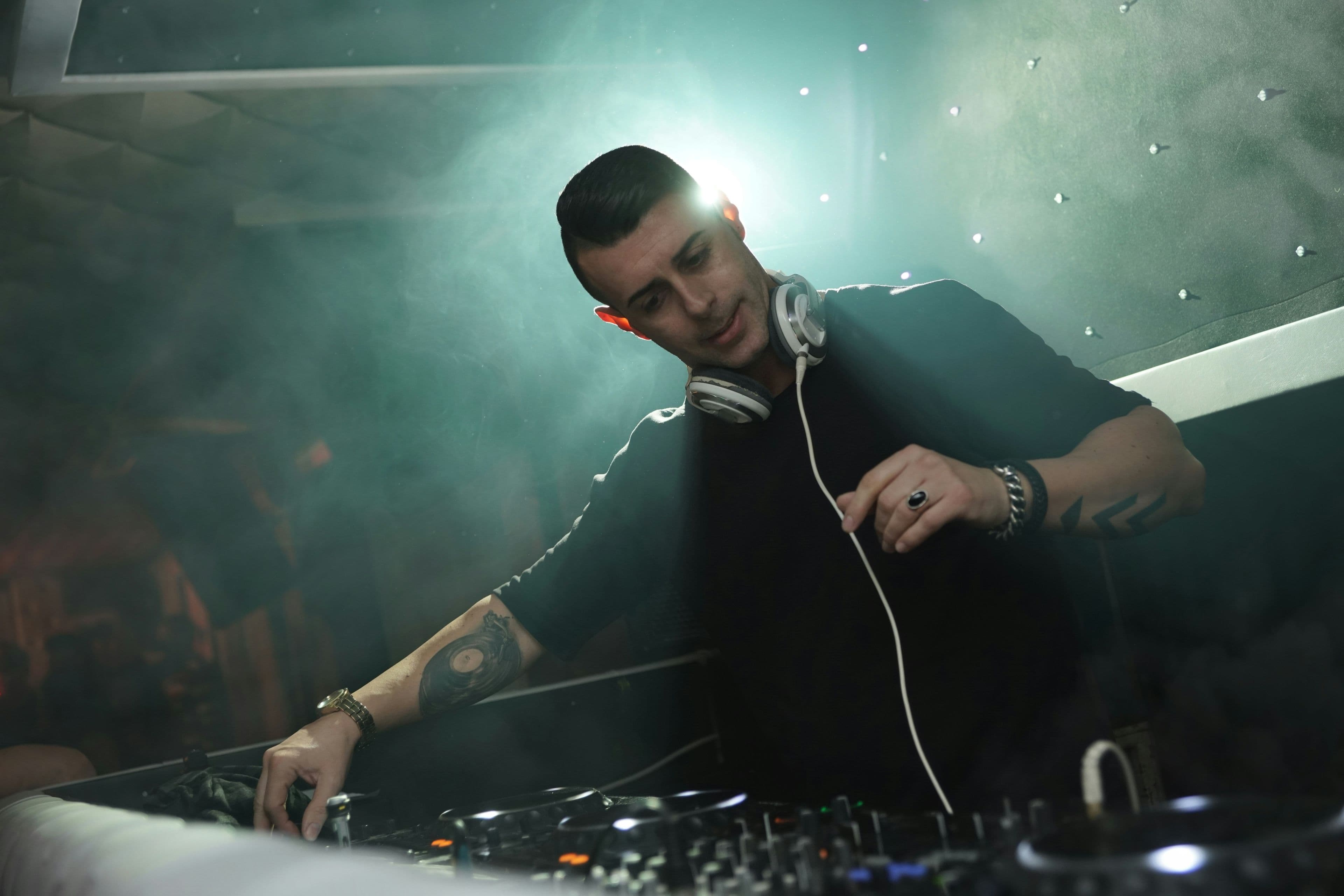 DJ mezclando música en la cabina durante un evento con luces y humo