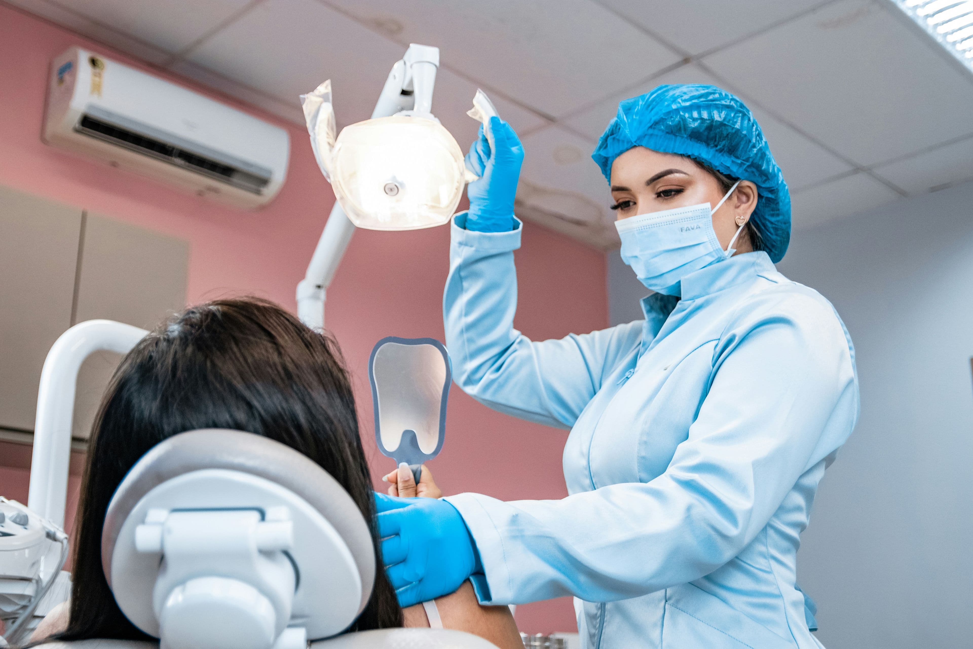 Dentista con cubrebocas y guantes atendiendo a una paciente en su consultorio
