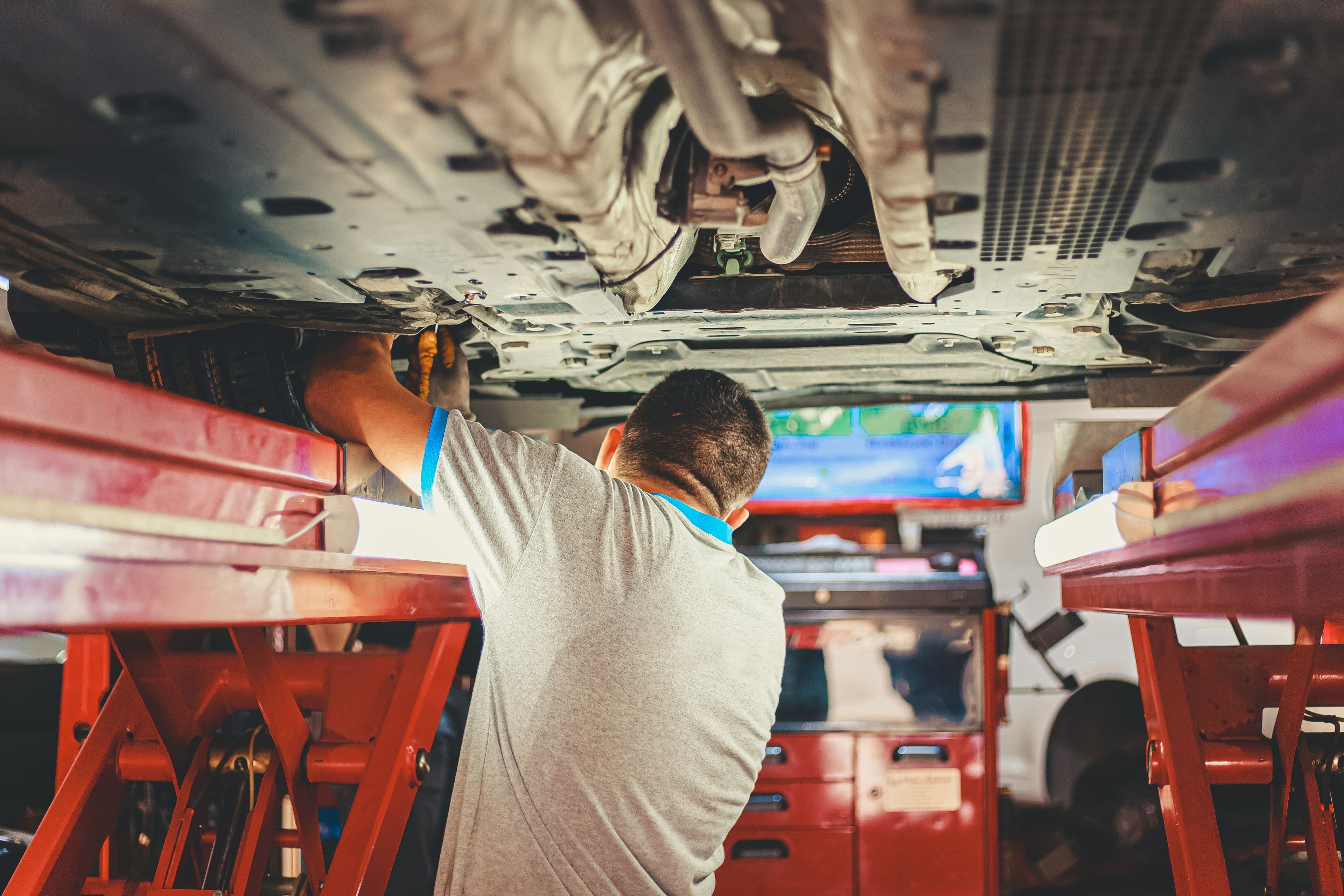 Técnico trabajando debajo de un auto levantado en un taller de servicio