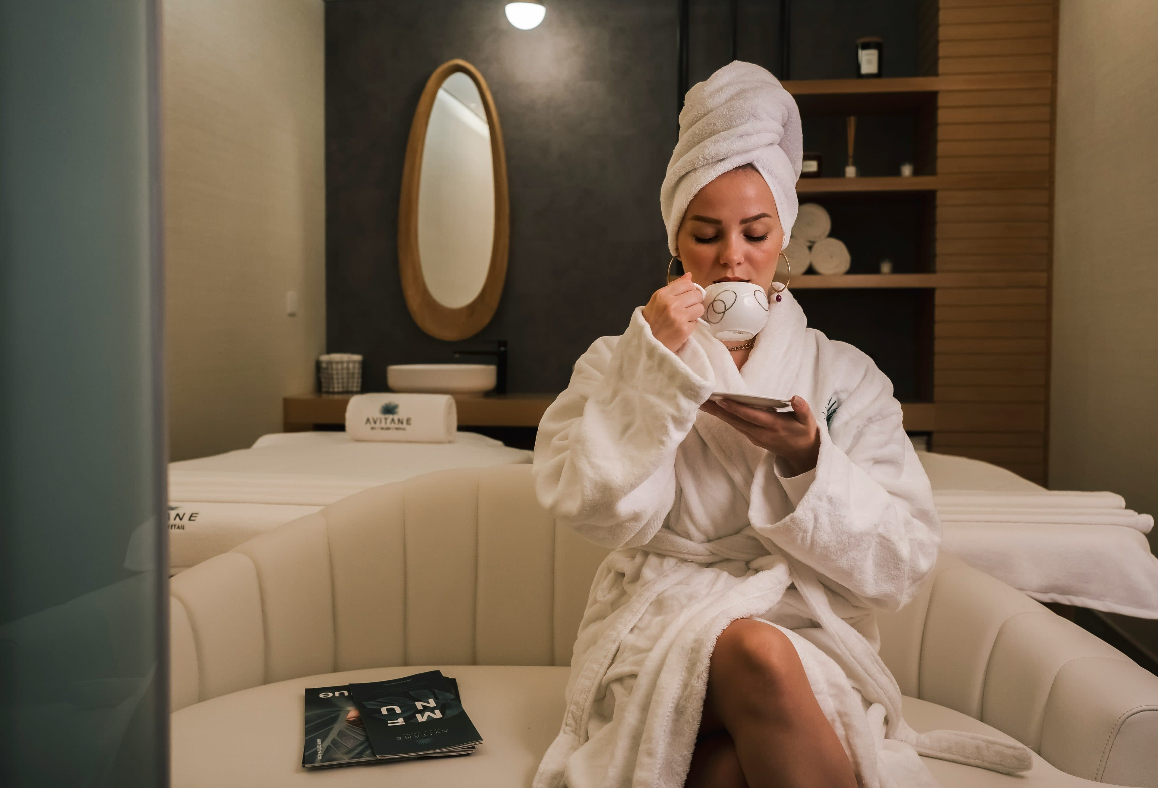 Clienta en bata y toalla disfrutando una bebida caliente en la sala de un spa